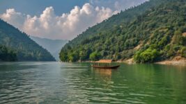 Traditional wooden boat floating on a serene green lake surrounded by forested hills under a partly cloudy sky