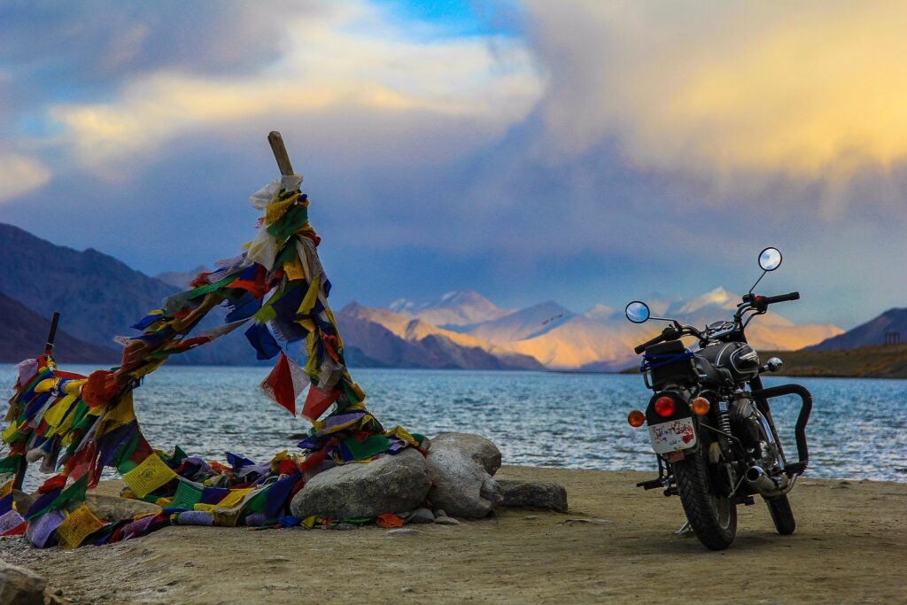 Motorbike parked near Pangong Lake in Ladakh with colorful Tibetan prayer flags and snow-capped mountains in the background