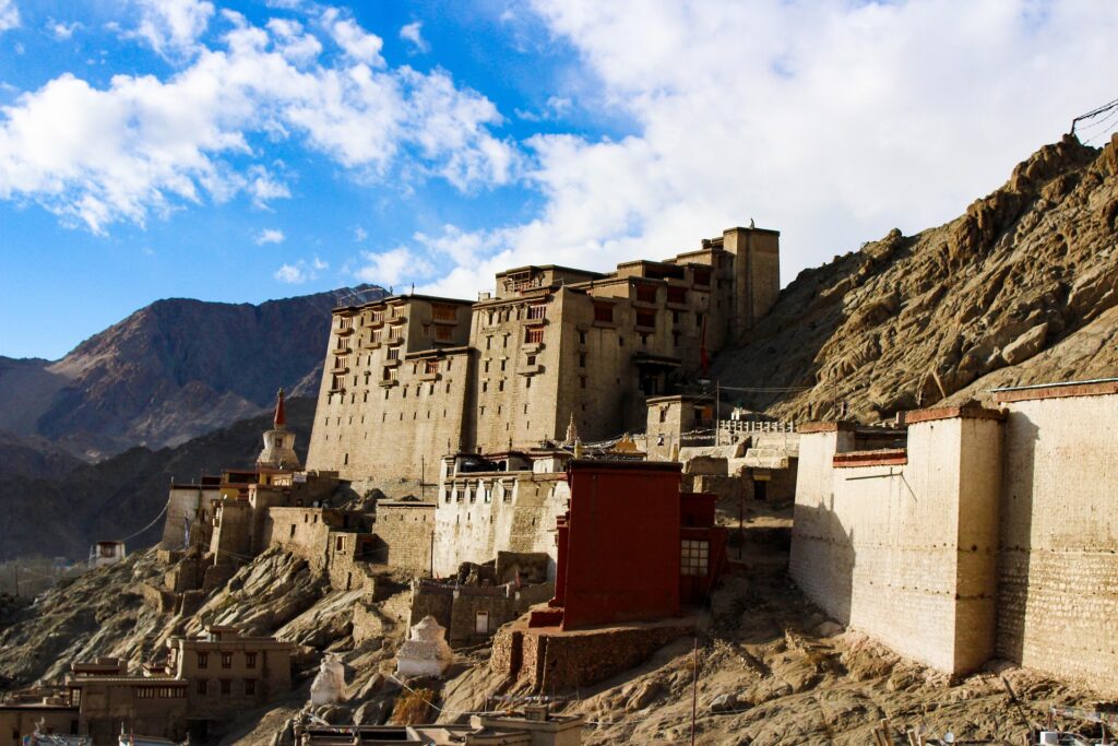 The old Leh Palace sits quietly on a rugged hillside in Ladakh, surrounded by dramatic mountains and a wide, open blue sky—it almost feels like it’s frozen in time.